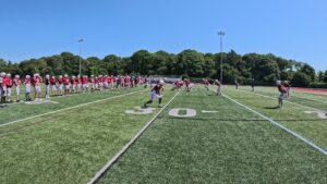 Football players warming up on a sunny field with trees in the background.