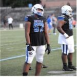 Football player in white and blue uniform standing on the field.