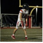 Football player walking on field during game night.