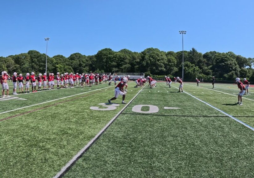 Football players warming up on a sunny field beside their team bench.